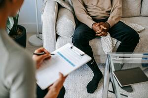 Man sitting in doctor's office while doctor holds clipboard. Photo by Alex Green: https://www.pexels.com/photo/crop-ethnic-client-discussing-problems-with-anonymous-psychologist-5699431/